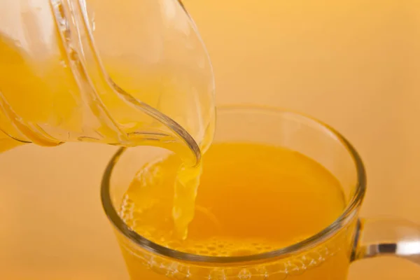 Jus d'orange versé dans un verre sur un fond d'orange — Photo