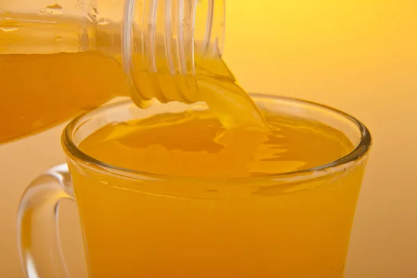 Suco de laranja derramando em um copo em um fundo laranja — Fotografia de Stock