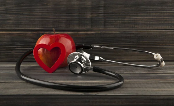 red apple, heart and stethoscope on a wooden background