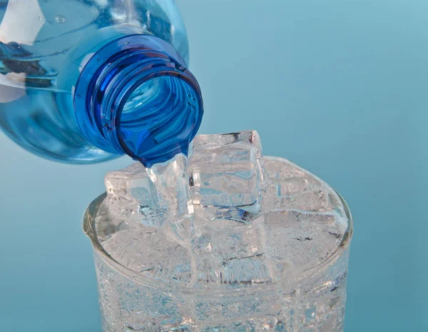 Fließendes Wasser in einem Glas mit Eis aus einer Flasche auf blauem Backgr — Stockfoto
