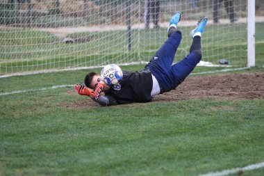 Odessa, Ukrayna - 2019 yılı: Yerel bir futbol takımının kalecisi, kötü bir futbol sahasında bölgesel bir derbi şampiyonasında oynarken kurtarıyor. Futbol golü, gol kalesi