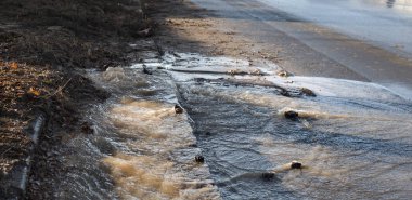 Acil Kanalizasyon. Yırtık bir yeraltı kanalizasyon borusundan su akıyor. Şehrin su şebekesinin kazası. Yerdeki bir çatlaktan yola akan bir çeşme.