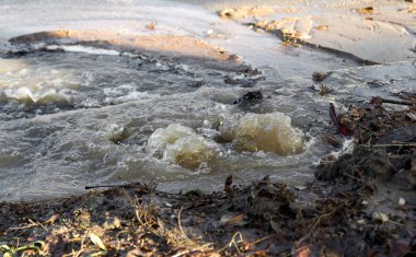Acil Kanalizasyon. Yırtık bir yeraltı kanalizasyon borusundan su akıyor. Şehrin su şebekesinin kazası. Yerdeki bir çatlaktan yola akan bir çeşme.