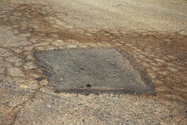 Çukurlu asfalt yolda hasar var. Kötü yol. Bozuk asfalt, bozuk otomobil yolu, çatlaklar, delikler, asfalttaki çukurlar.