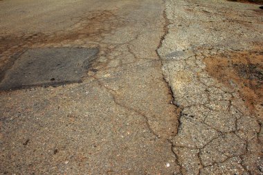 Çukurlu asfalt yolda hasar var. Kötü yol. Bozuk asfalt, bozuk otomobil yolu, çatlaklar, delikler, asfalttaki çukurlar.