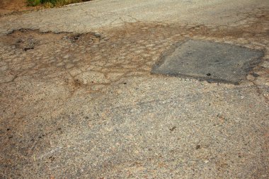 Çukurlu asfalt yolda hasar var. Kötü yol. Bozuk asfalt, bozuk otomobil yolu, çatlaklar, delikler, asfalttaki çukurlar.