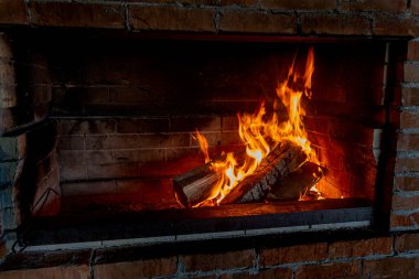 Kaliteli bir şöminede yangın. Şöminede ateşte et kızartmak için odun ve kömür yanıyor.