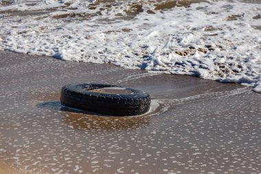 Kumsalda eski araba lastikleri, kumsalda deniz ve deniz kirliliği olan araba lastikleri, kumlara saplanmış eski bir araba lastiğinin görüntüsü..