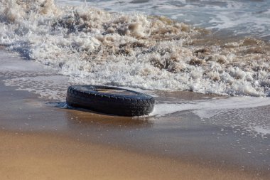 Kumsalda eski araba lastikleri, kumsalda deniz ve deniz kirliliği olan araba lastikleri, kumlara saplanmış eski bir araba lastiğinin görüntüsü..