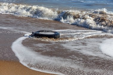 Kumsalda eski araba lastikleri, kumsalda deniz ve deniz kirliliği olan araba lastikleri, kumlara saplanmış eski bir araba lastiğinin görüntüsü..