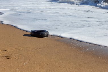 Kumsalda eski araba lastikleri, kumsalda deniz ve deniz kirliliği olan araba lastikleri, kumlara saplanmış eski bir araba lastiğinin görüntüsü..