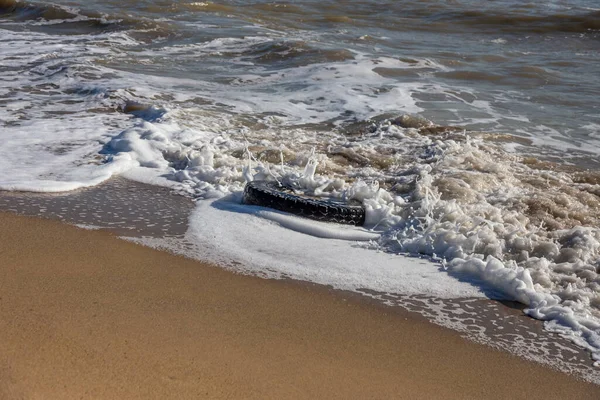 Old car tires on the beach,Water and sea coast pollution car tires on sand beach,An image of an old car tire ingrown into the sand.Old car tires with seaweed stuck on.