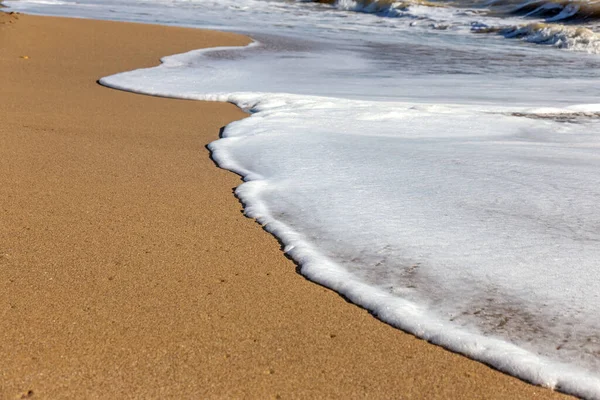 A soft sea wave rolls onto the sand of the beach. Seascape waves on the coast