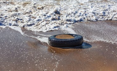 Kumsalda eski araba lastikleri, kumsalda deniz ve deniz kirliliği olan araba lastikleri, kumlara saplanmış eski bir araba lastiğinin görüntüsü..