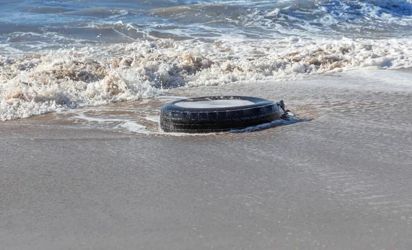 Old car tires on the beach,Water and sea coast pollution car tires on sand beach,An image of an old car tire ingrown into the sand.Old car tires with seaweed stuck on.