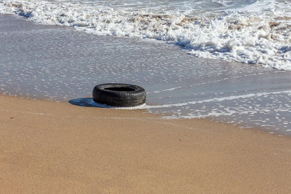 Old car tires on the beach,Water and sea coast pollution car tires on sand beach,An image of an old car tire ingrown into the sand.Old car tires with seaweed stuck on.