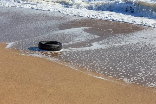 Old car tires on the beach,Water and sea coast pollution car tires on sand beach,An image of an old car tire ingrown into the sand.Old car tires with seaweed stuck on.