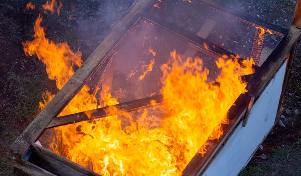 Fire coils over a burnt building. A pile of coals at the site of a burnt shed. Bright flames, flying ashes of a burning wooden building during a fire