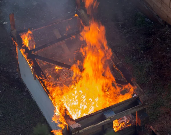 Fire coils over a burnt building. A pile of coals at the site of a burnt shed. Bright flames, flying ashes of a burning wooden building during a fire