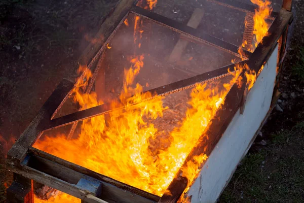 Fire coils over a burnt building. A pile of coals at the site of a burnt shed. Bright flames, flying ashes of a burning wooden building during a fire