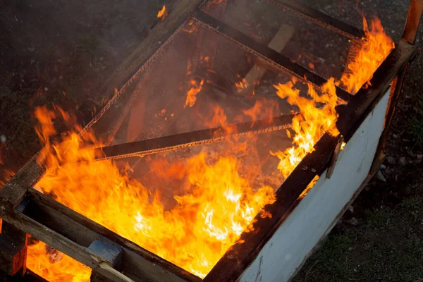 Fire coils over a burnt building. A pile of coals at the site of a burnt shed. Bright flames, flying ashes of a burning wooden building during a fire