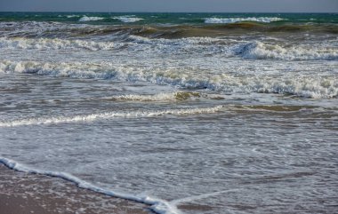Bir deniz dalgası sahildeki bir kumsalda köpükle koşuyor. Günbatımı renklerinde deniz manzarası. Tasarım ve dekorasyon için güzel doğal arkaplan