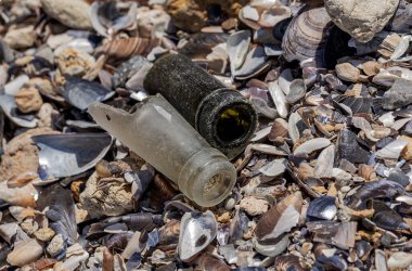 Deniz kıyısındaki kırık şişelerden gelen tehlikeli cam parçaları. Sahilde cam tehlikeli çöp.