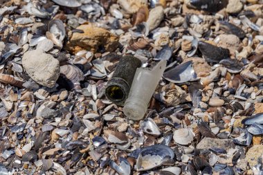 Deniz kıyısındaki kırık şişelerden gelen tehlikeli cam parçaları. Sahilde cam tehlikeli çöp.