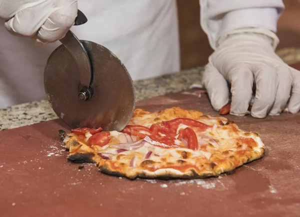 Chef cutting a pizza into slices using a wheel cutter — Stock Photo, Image