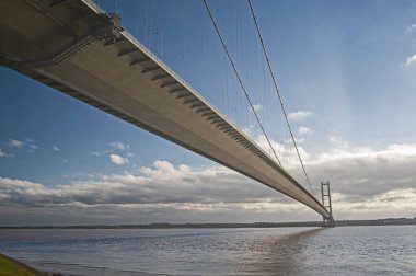 Geniş nehir kıyılarını kaplayan büyük asma köprü açık bir günde mavi gökyüzü ve bulutlarla