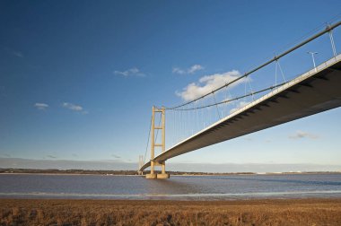 Geniş nehir kıyılarını kaplayan büyük asma köprü açık bir günde mavi gökyüzü ve bulutlarla