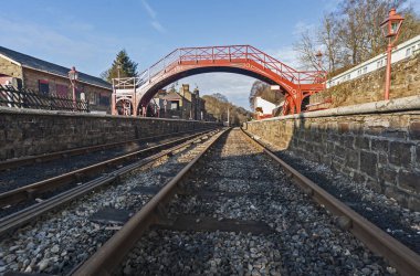 Ayak köprüsü olan eski bir köy tren istasyonunun raylarına bakın.