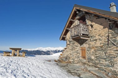 Dağlık yamaçlarda uzak taş evlerle kaplı panoramik kar manzarası
