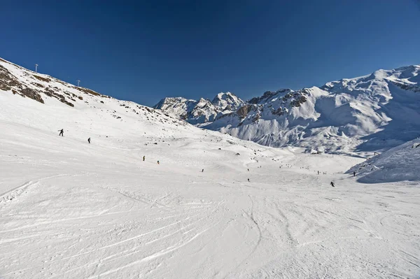 冬のアルペンマウンテンリゾートでスキー場の斜面の下に行くスキーヤーとのパノラマ風景の谷の景色 — ストック写真