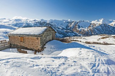 Dağlık yamaçlarda uzak taş evlerle kaplı panoramik kar manzarası
