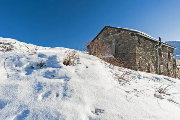 遠くの石造りの家の住居と高山の山の斜面に覆われた雪のパノラマビュー — ストック写真