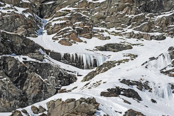 Rugged alpine rocky mountainside landscape with frozen waterfall covered in snow and ice