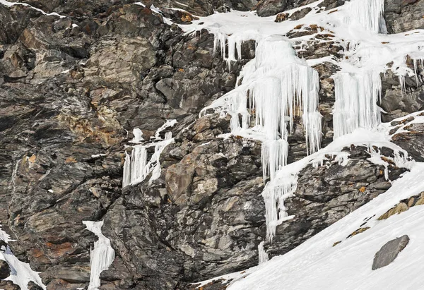 Rugged alpine rocky mountainside landscape with frozen waterfall covered in snow and ice