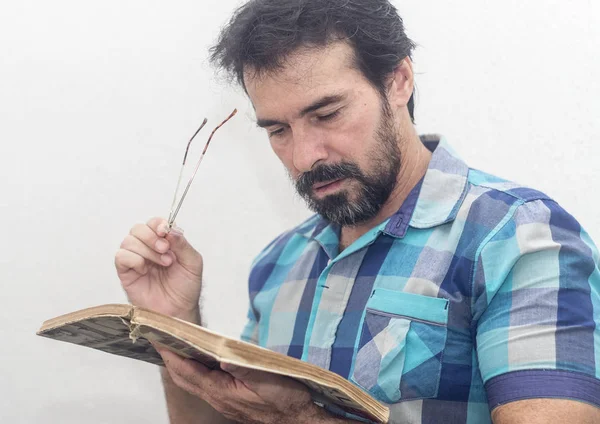 A white man with a black beard, some gray hairs, glasses, looking at a book, wearing a blue plaid shirt — Stock Photo, Image