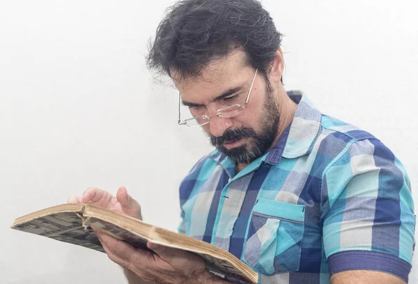 A white man with a black beard, some gray hairs, glasses, looking at a book, wearing a blue plaid shirt — Stock Photo, Image