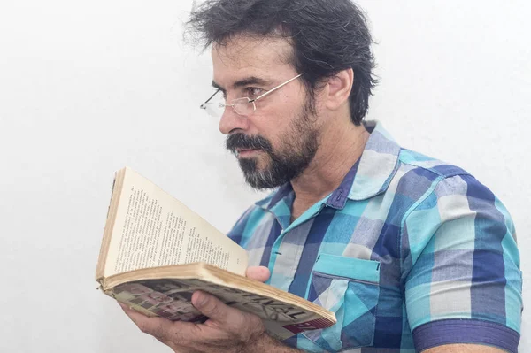 A white man with a black beard, some gray hairs, glasses, looking at a book, wearing a blue plaid shirt — Stock Photo, Image