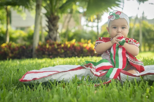 Bebê branco muito bonito, sentado na grama, vestindo vestido colorido mexicano, fita branca e gravata borboleta na cabeça. Gesticulando e expressando emoções diversas, originais e muito agradáveis, engraçadas, sugestivas. Muito natural e autêntico. Sol brilhante — Fotografia de Stock