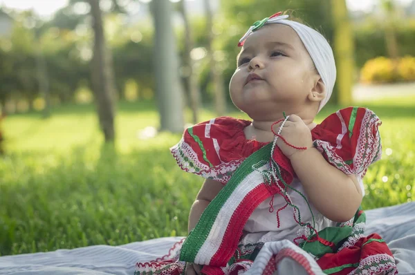 Bebita blanca muy hermosa, sentada en la hierba, con vestido de colores mexicanos, cinta blanca y lazo de colorines en la cabeza. Gesticulando y expresando emociones diversas, originales y muy simpticas, graciosas, sugerentes. Çok doğal sonbahar.