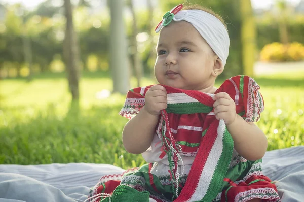 Bebita blanca muy hermosa, sentada en la hierba, con vestido de colores mexicanos, cinta blanca y lazo de colorines en la cabeza. Gesticulando y expresando emociones diversas, originales y muy simpticas, graciosas, sugerentes. Çok doğal sonbahar.
