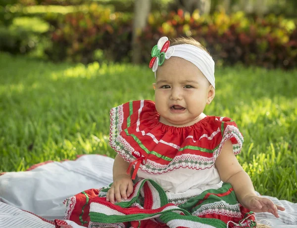 Bebita blanca muy hermosa, sentada en la hierba, con vestide colores mexicanos, cinta blanca y lazo de colorines en la cabeza. Gesticulando y expresando emociones diversas, originales y muy simpticas, graciosa, sugerentes. Muy natural y autn — Fotografia de Stock