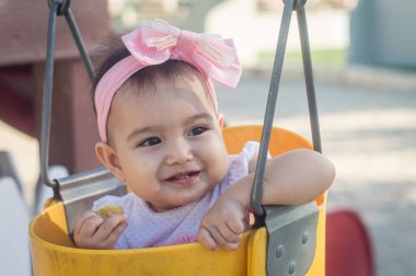 Bir yaşında bebek, sarı salıncak ve pembe fiyonk