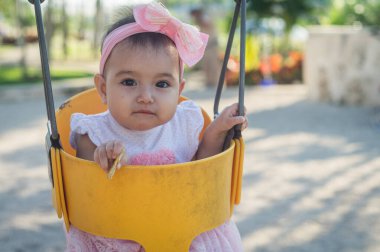 Bir yaşında bebek, sarı salıncak ve pembe fiyonk