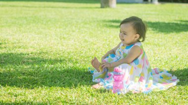 Çimlerin üzerinde oturan renkli elbiseli küçük kız.