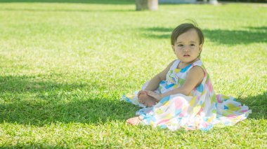 Çimlerin üzerinde oturan renkli elbiseli küçük kız.