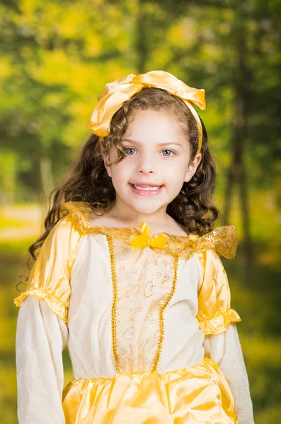 Schattig klein meisje dragen mooie gele jurk met bijpassende hoofdband, poseren voor de camera, groene bos achtergrond — Stockfoto